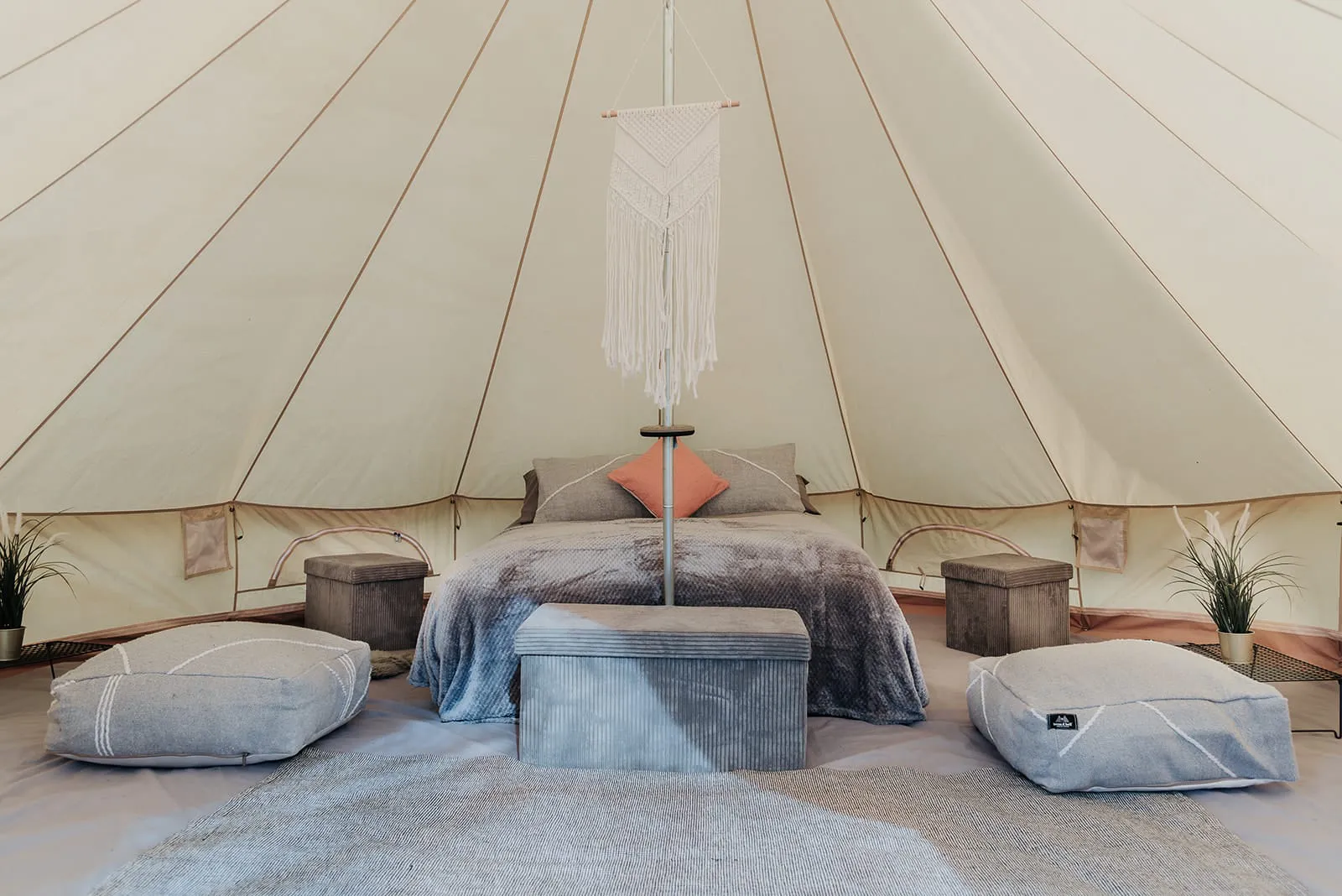 Inside a bell tent: camp beds with bedding, full-circle flooring and centre-pole lighting.